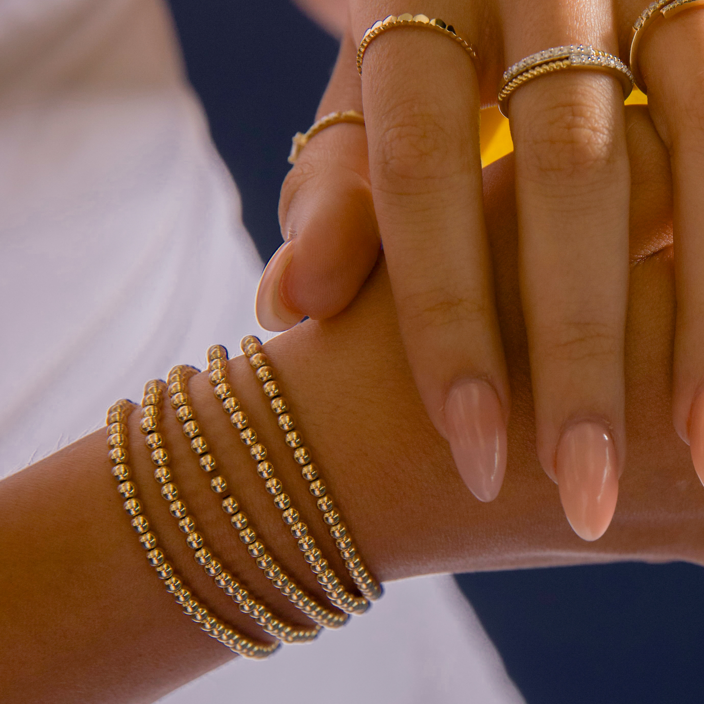 Styled hands wearing Gold Club by Shannon Hudson rings with 14k gold-filled LustraFlex™ bead bracelets