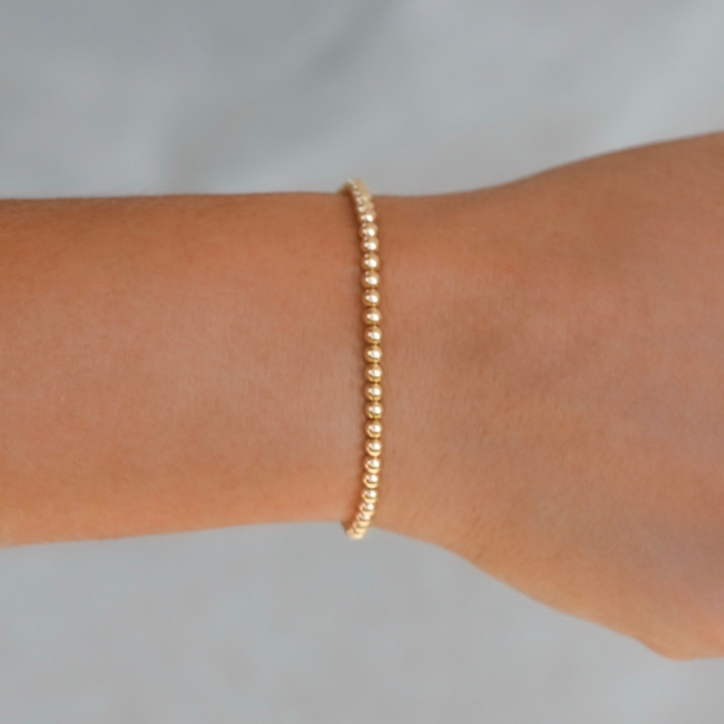 Gold bracelet on a person's wrist against a light gray background. 3mm Gold LustraFlex™ Bracelet