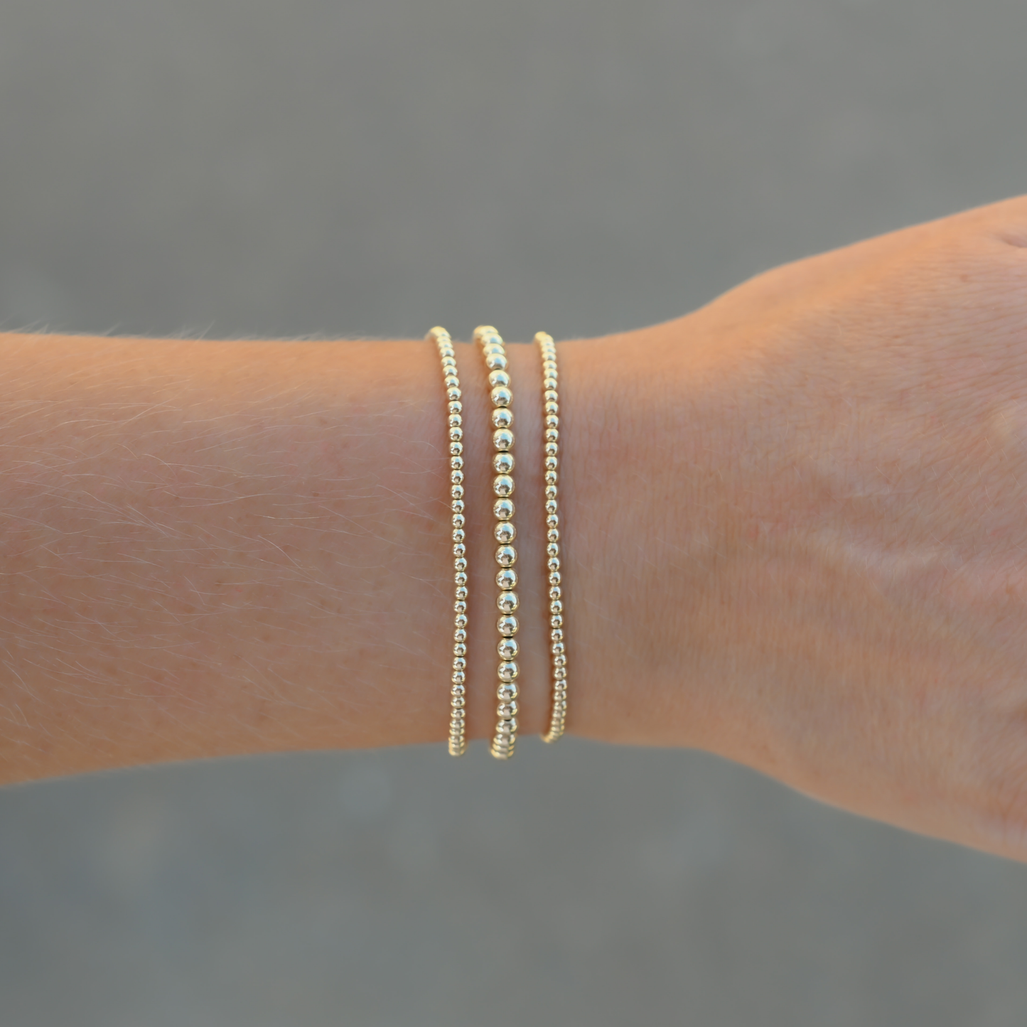 Set of three Gold Club by Shannon Hudson Gold LustraFlex™ Bracelets on a blurred background