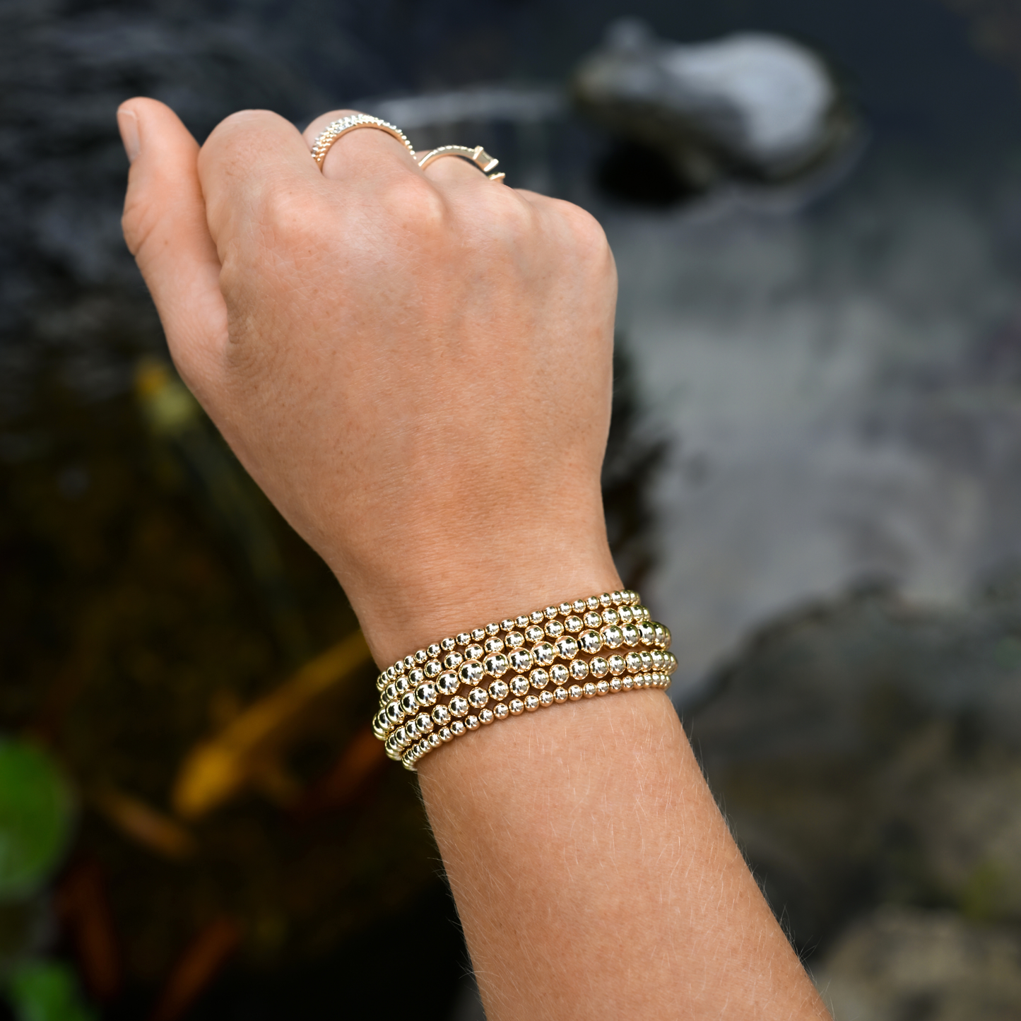 Close up of Gold Club’s LustraFlex™ bracelet worn on wrist with rings shown a blurred background.