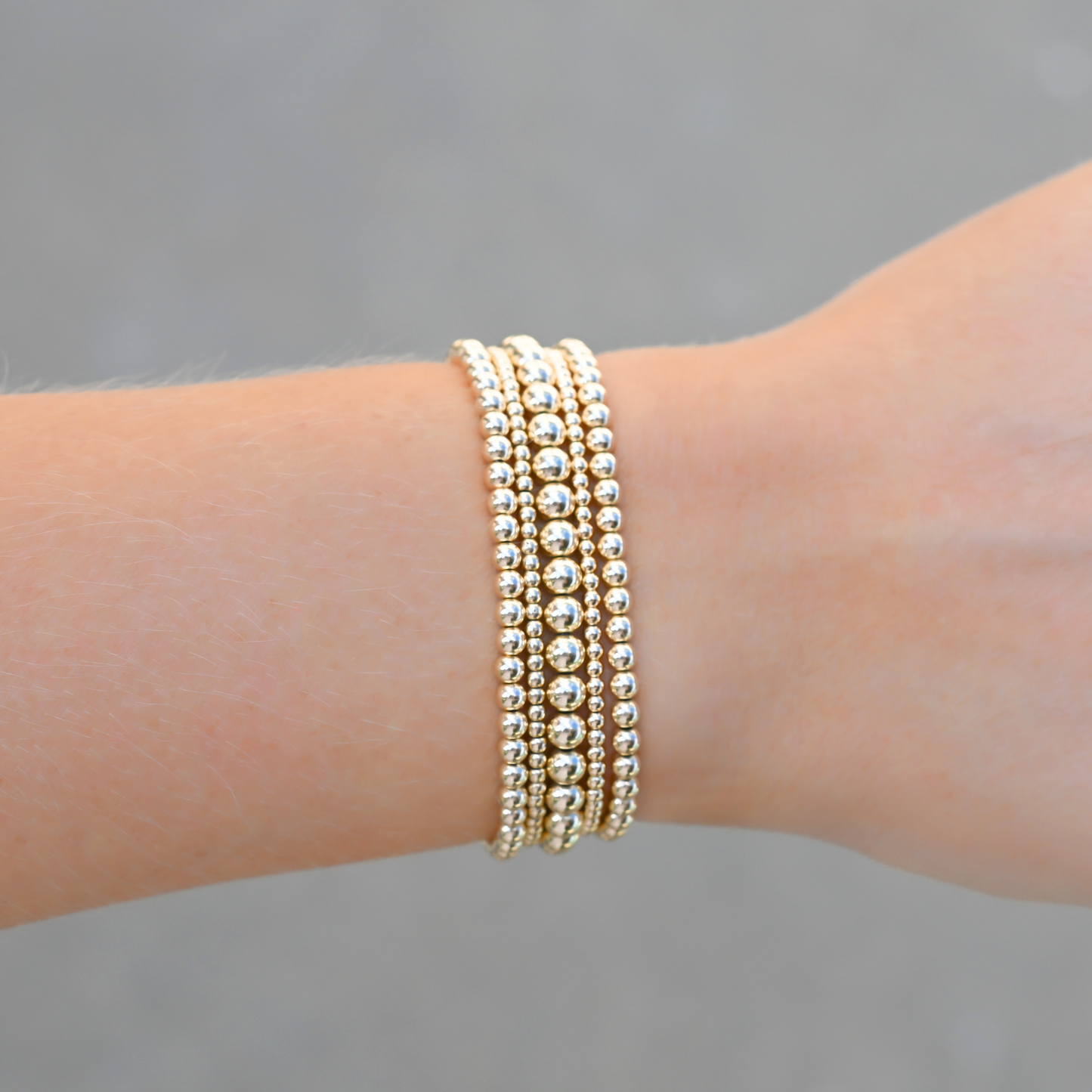 Stack of Gold Club by Shannon Hudson gold filled LustraFlex™ bracelets on a wrist against a gray background