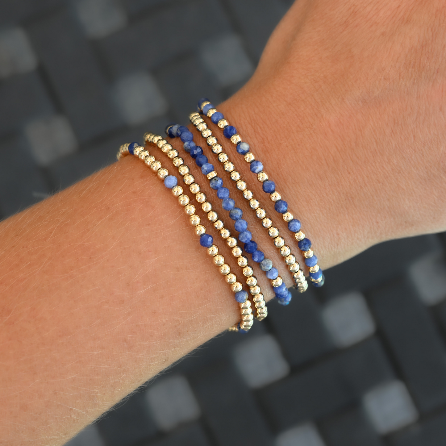 Five gold-filled and kyanite LustraFlex™ bracelets from Gold Club by Shannon Hudson, styled on an active woman’s wrist with rings.