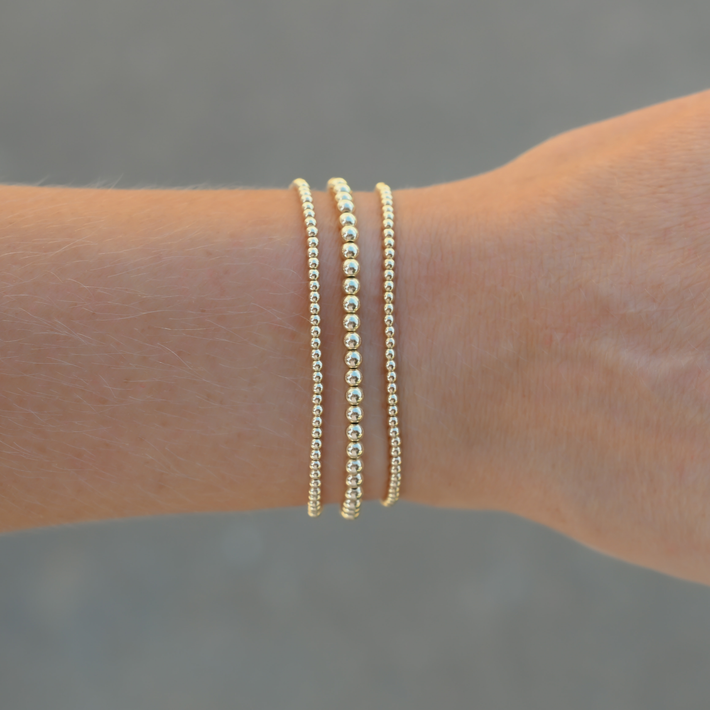 Two gold bracelets on a wrist with a blurred background