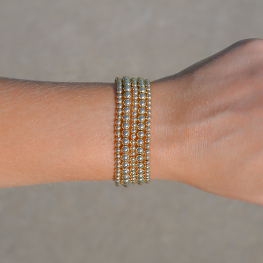 Close-up of a wrist wearing multiple gold-filled beaded bracelets from Gold Club on a neutral background