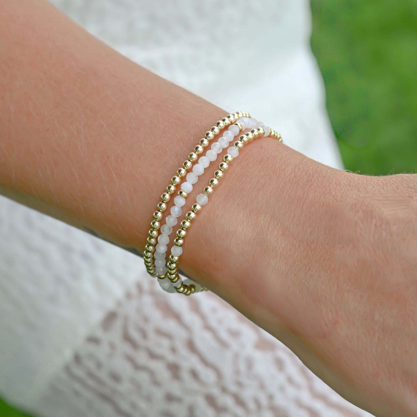 Layered white moonstone and gold-filled bracelets in natural light