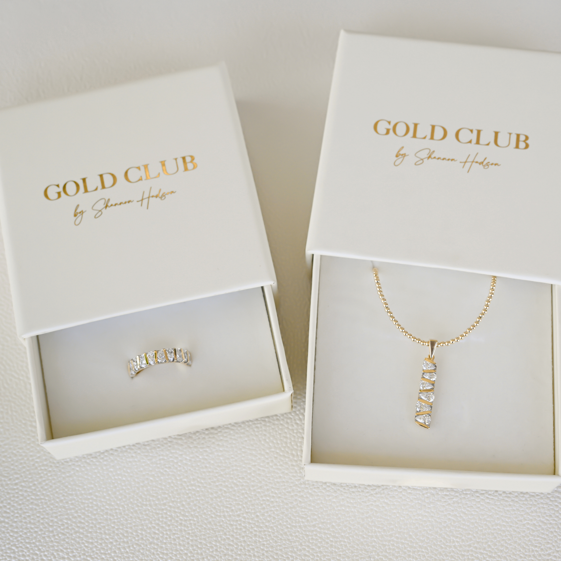 Gold Club by Shannon Hudson fine jewelry in display boxes featuring a lab-grown diamond ring and a 14k gold diamond bar pendant