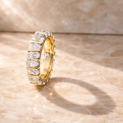 Gold eternity band with pear shaped diamonds on a beige marble