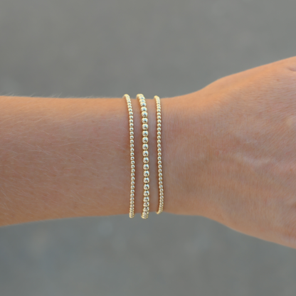 Set of three Gold Club by Shannon Hudson Gold LustraFlex™ Bracelets on a blurred background