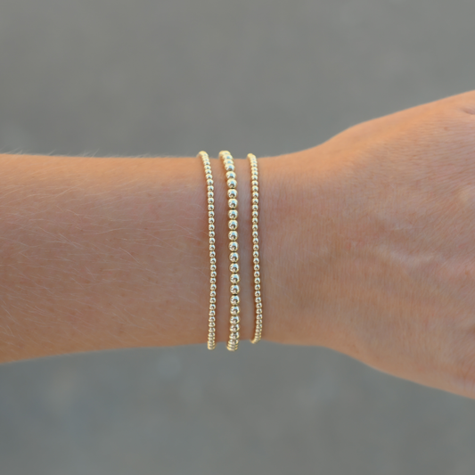 Set of three Gold Club by Shannon Hudson Gold LustraFlex™ Bracelets on a blurred background
