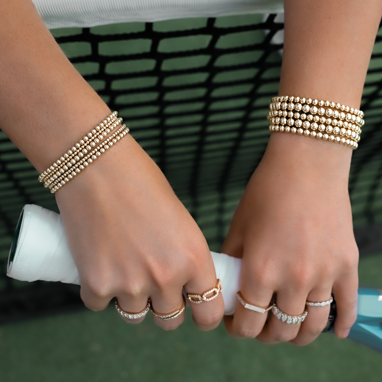Gold-filled bracelets and rings from Gold Club by Shannon Hudson displayed on a tennis court—jewelry designed for active lifestyles.