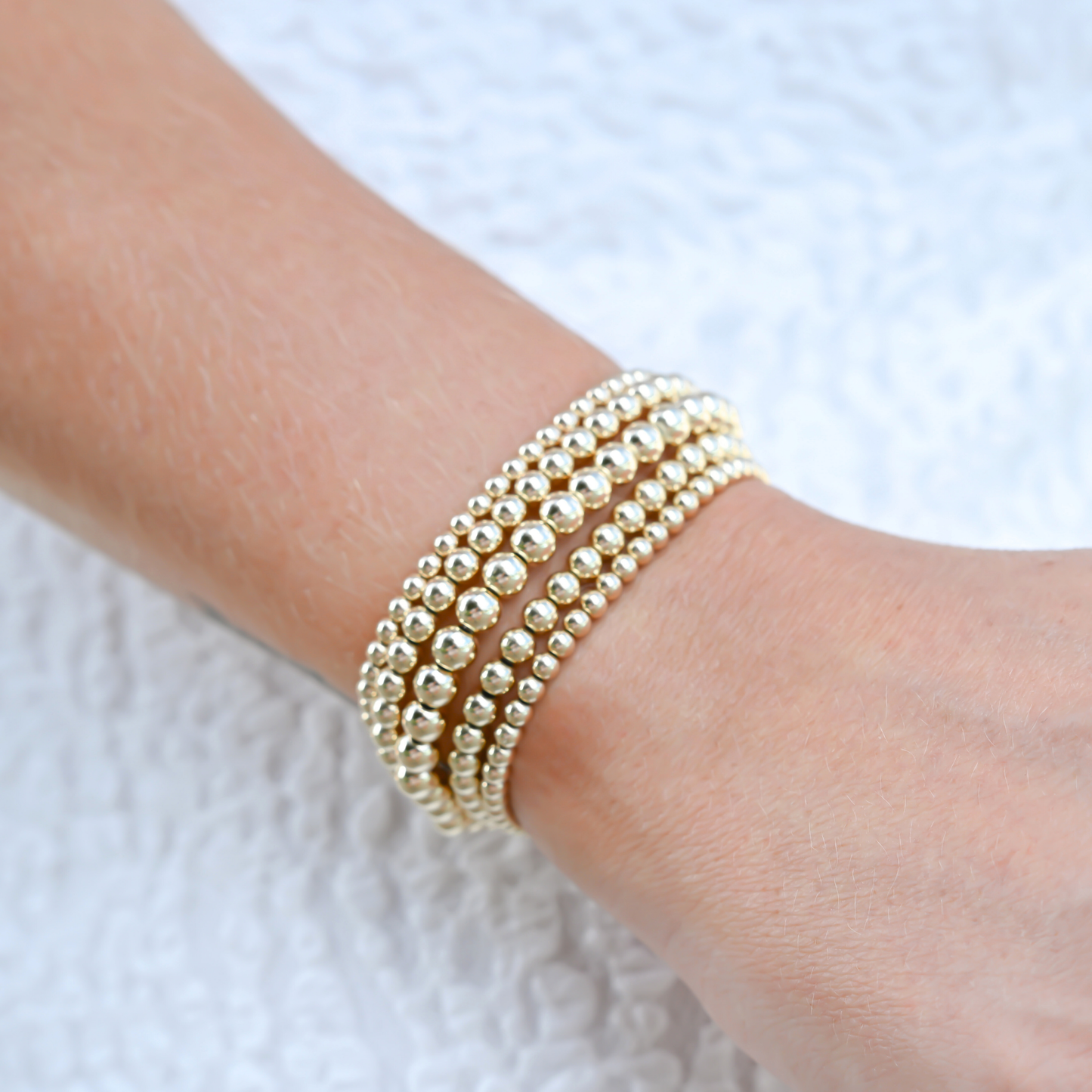 Stack of Gold Club bracelets on activewear set, highlighting LustraFlex™ gold beaded band.