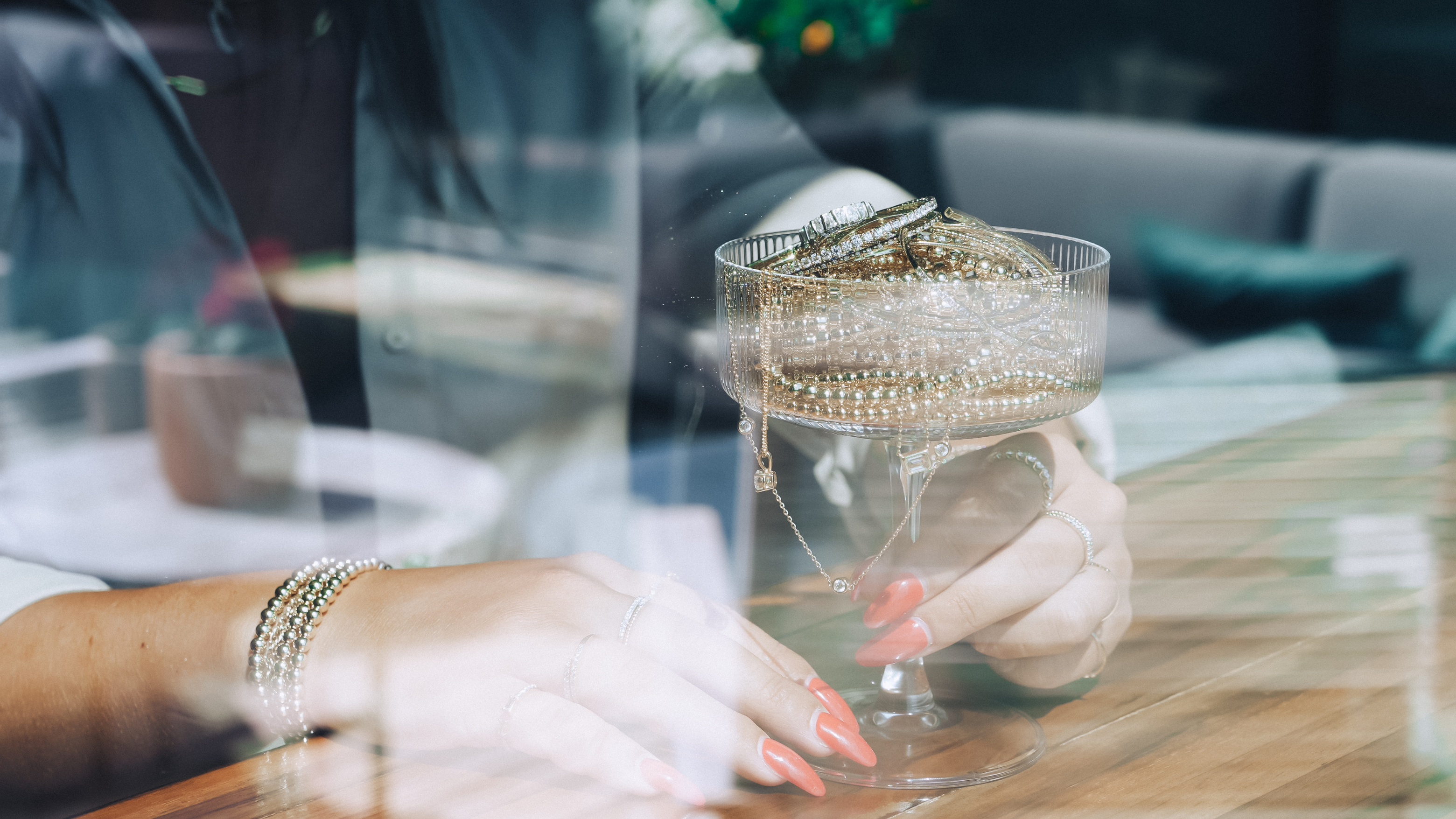 A woman holding a martini glass filled with Gold Club by Shannon Hudson jewelry.
