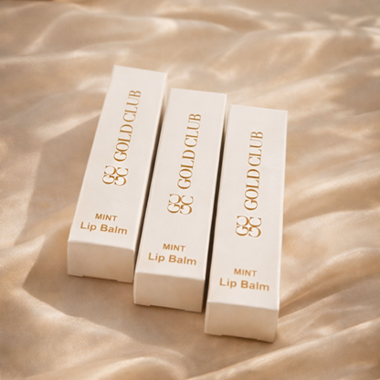 Three Gold Club Mint Lip Balm containers on a beige fabric background