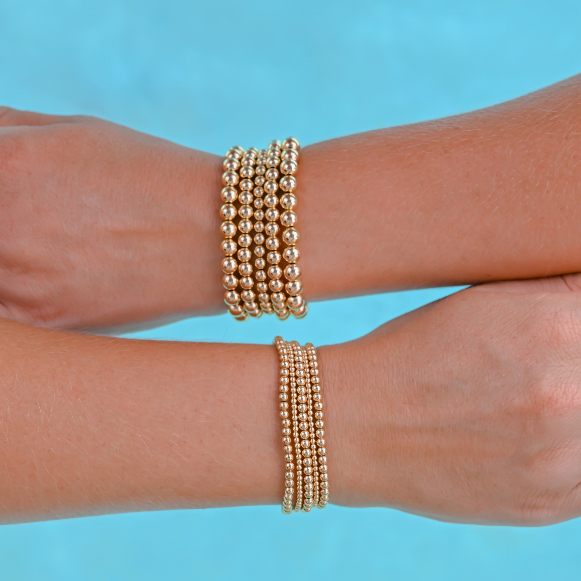 Two arms wearing gold filled LustraFlex™ beaded bracelets in a pool Gold Club by Shannon Hudson