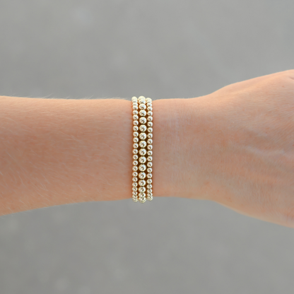 Signature Stack Gold Club by Shannon Hudson bracelet on a wrist against a gray background