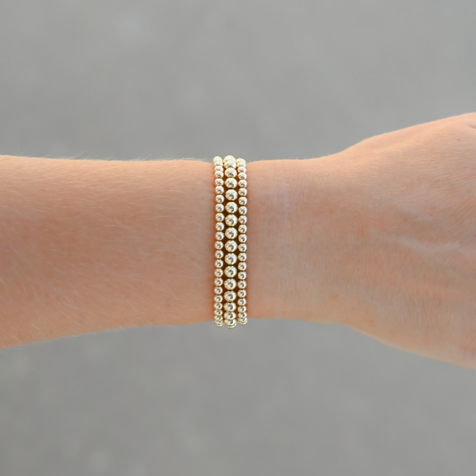 Signature Stack Gold Club by Shannon Hudson bracelet on a wrist against a gray background