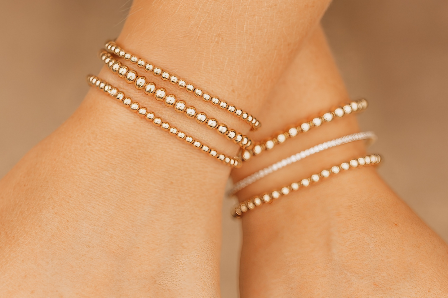 Close-up of a person's wrists with multiple LustraFlex™ bracelets and rings on a beige background
