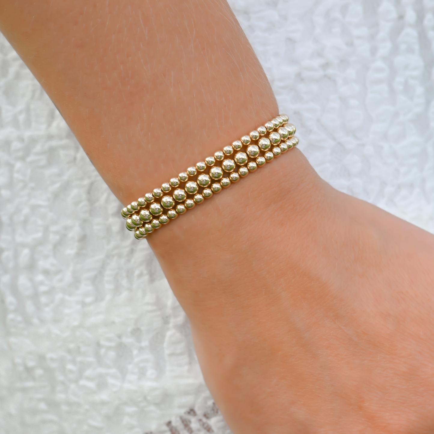 Stack of Gold Club by Shannon Hudson Gold LustraFlex™ Bracelets styled on a wrist with a white dress
