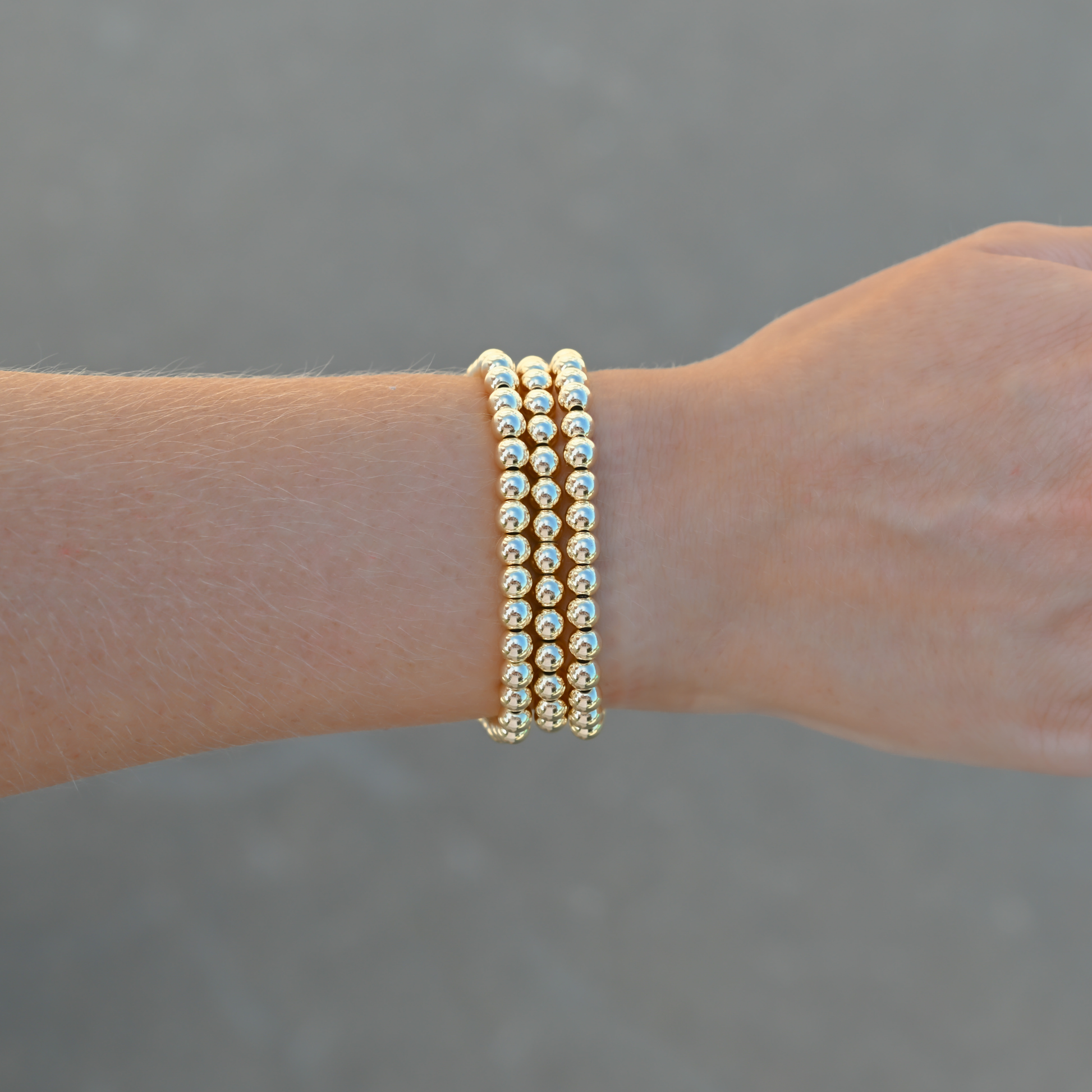 Gold-filled beaded bracelets featuring LustraFlex™ technology styled on a wrist with neutral background