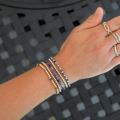 Five gold-filled and kyanite LustraFlex™ bracelets from Gold Club by Shannon Hudson, styled on an active woman’s wrist with rings. 