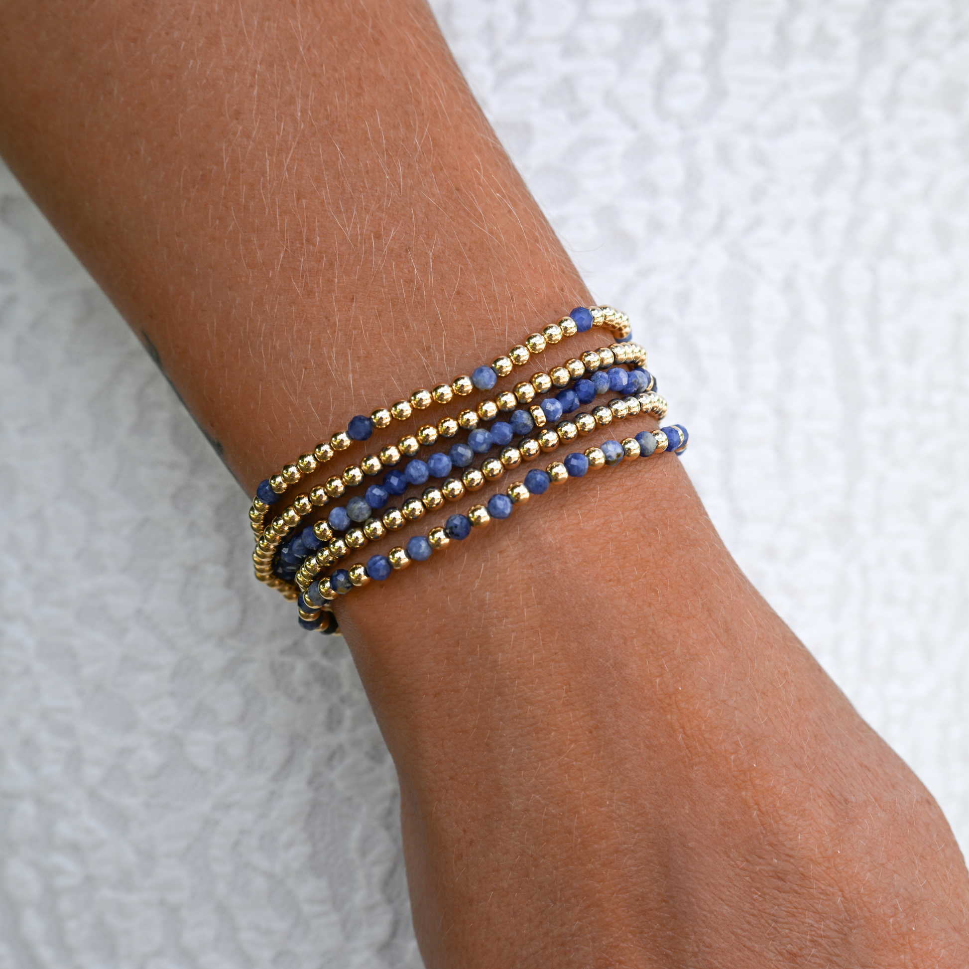 Active lifestyle jewelry – LustraFlex™ gold and gemstone bracelet styled on a woman's wrist with a white dress.