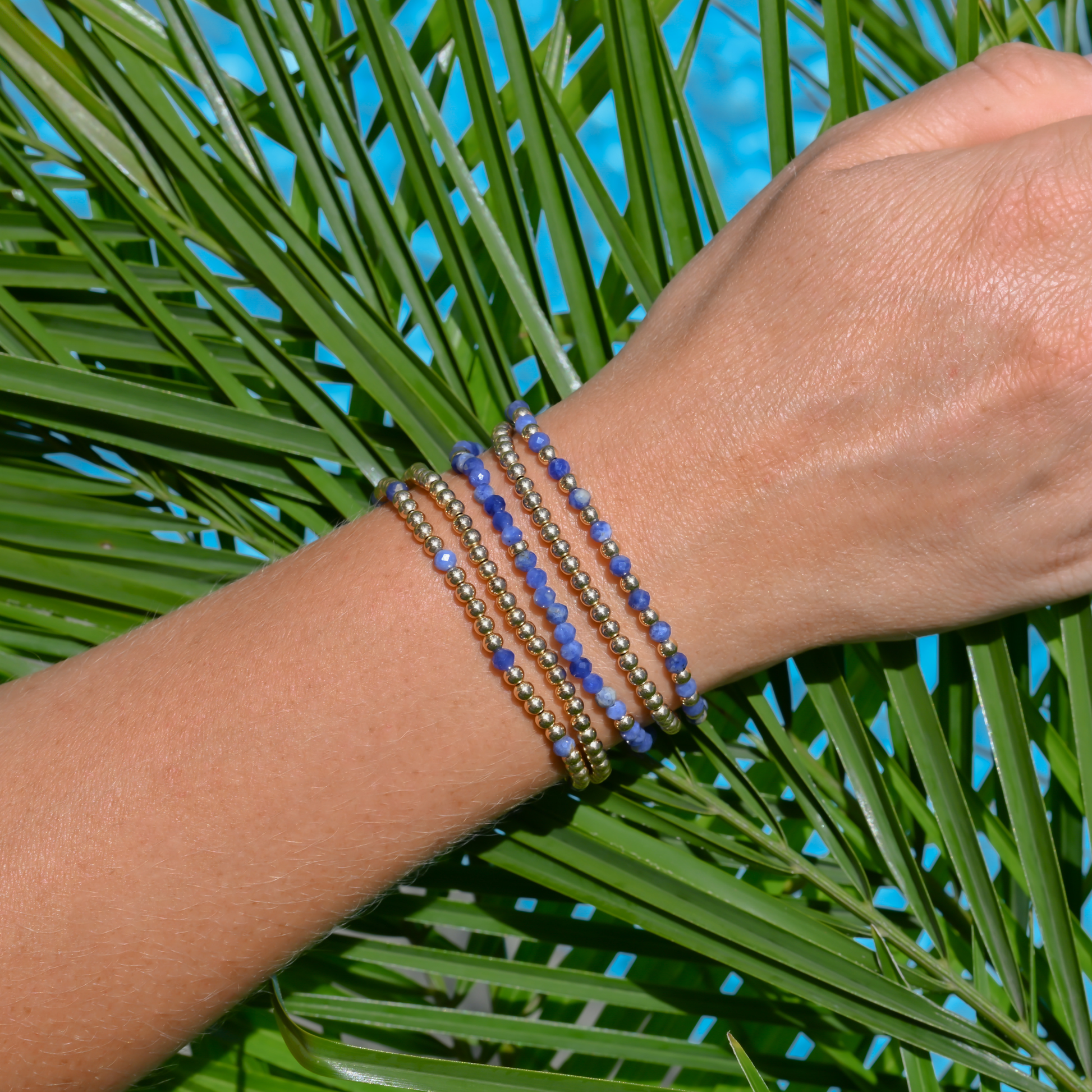 LustraFlex™ gold-filled beaded bracelet stack by Gold Club on palm leaves.