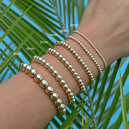 Gold filled LustraFlex™ bracelets on a wrist with size labels against a palm leaf background