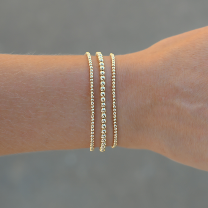 Two gold bracelets on a wrist with a blurred background