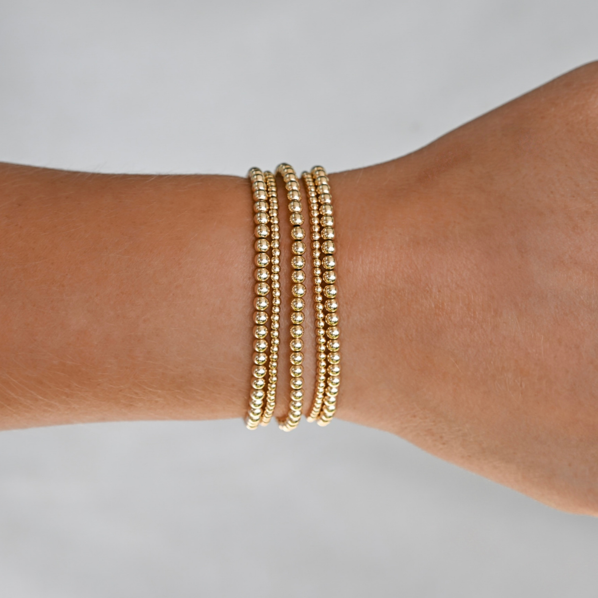 Gold beaded bracelets on a wrist against a neutral background