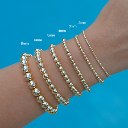 Gold-filled LustraFlex™ bracelet size guide from Gold Club by Shannon Hudson stacked on a woman’s wrist in a pool.