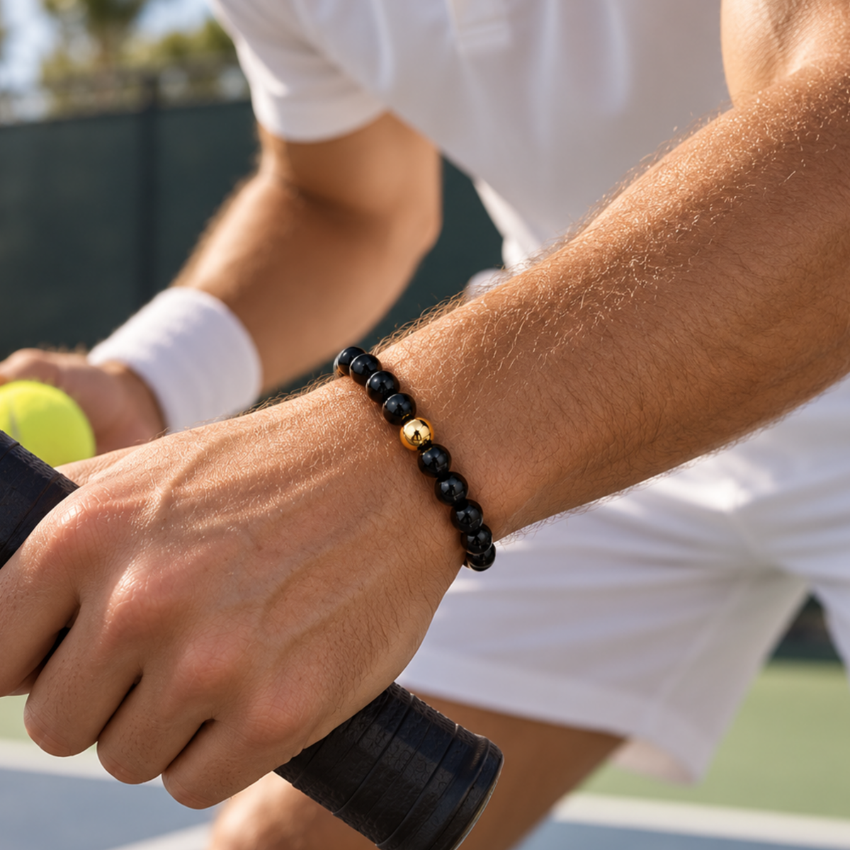 Men’s polished black natural stone bead bracelet with gold-filled bead on a tennis court. jewelry you can play tennis in.