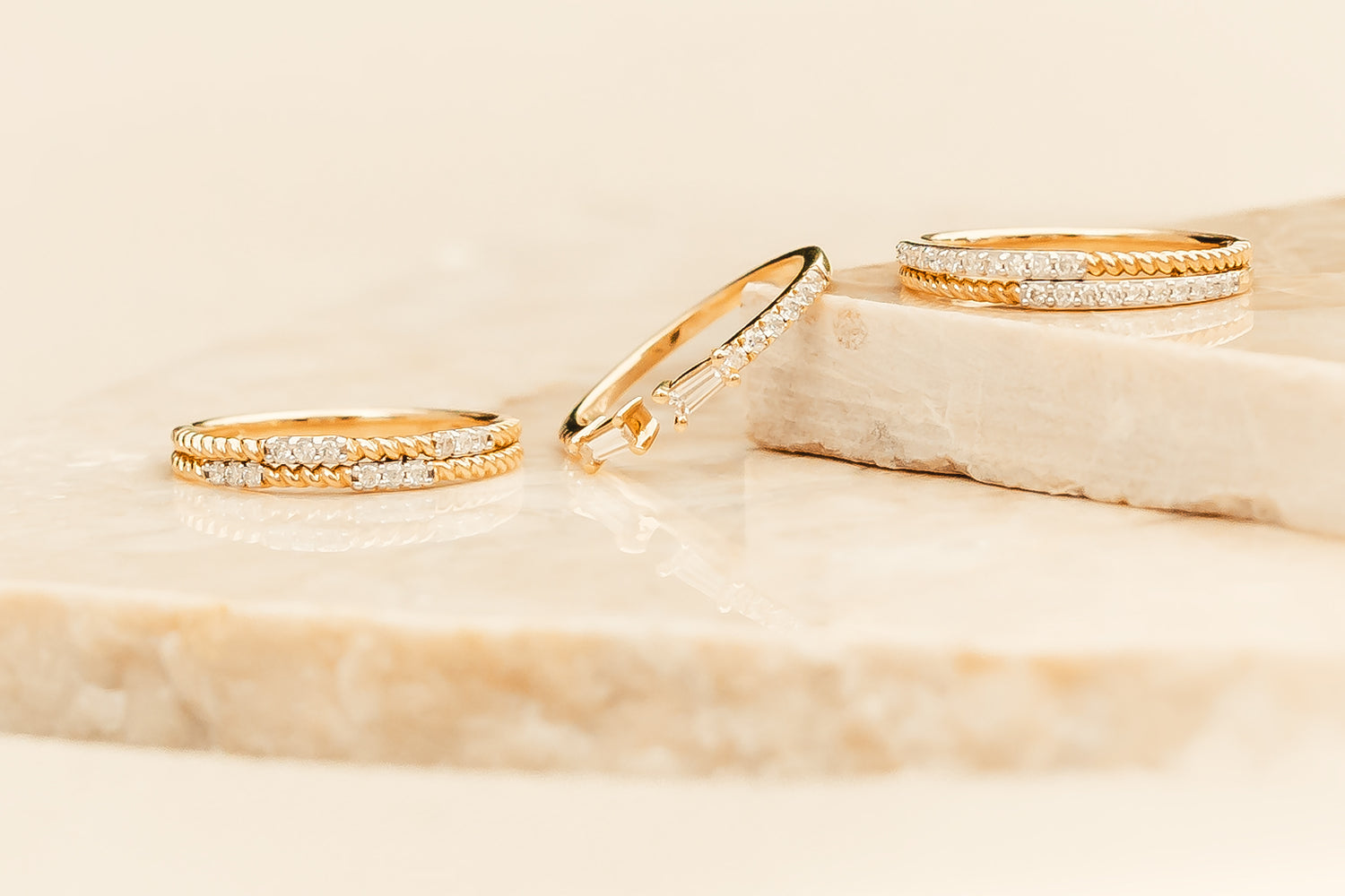 Three gold rings from Gold Club by Shannon Hudson with diamond accents on a marble surface