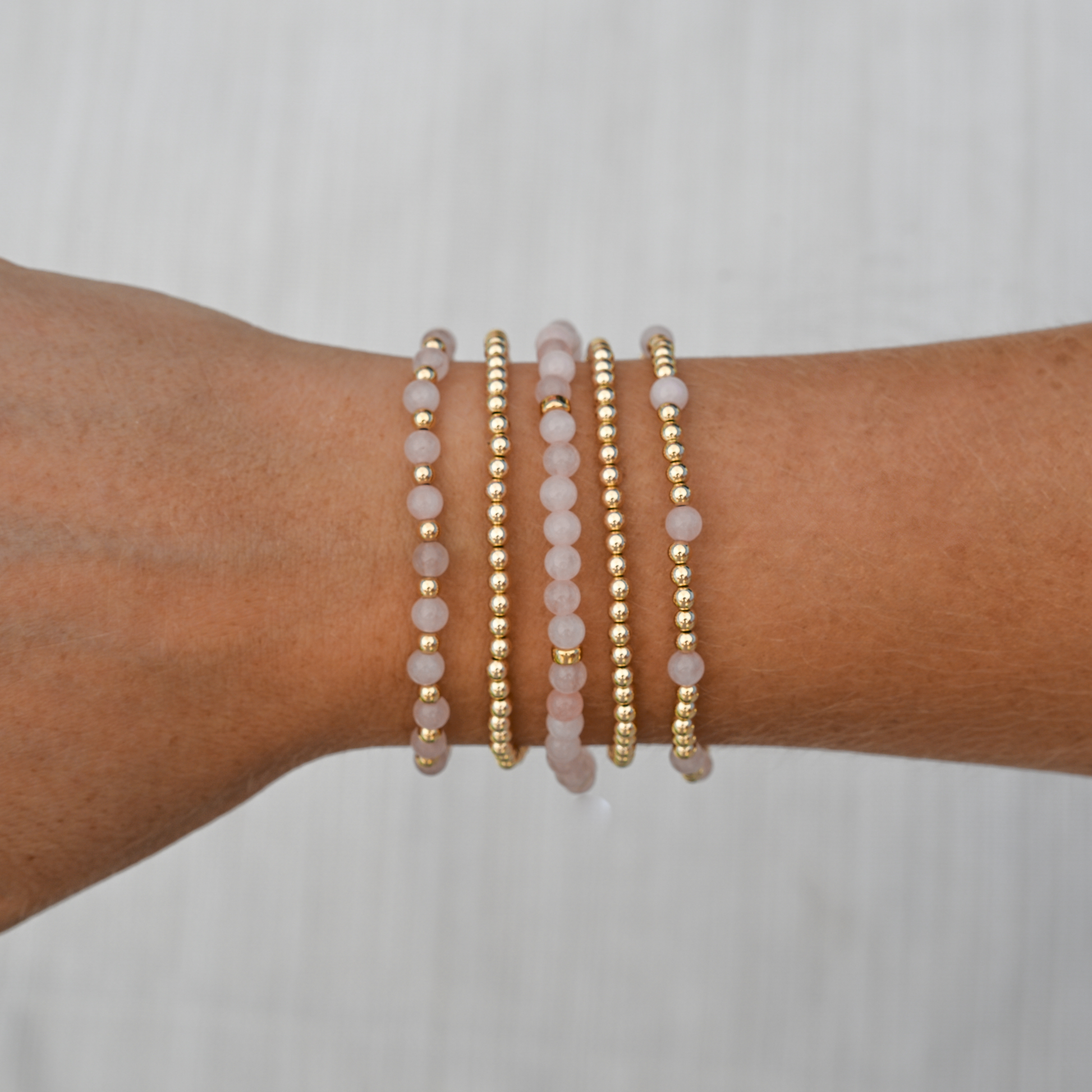 Pink Quartz Mini Stack styled on wrist in sunlight, featuring Arc, Muse, and Sun designs from the GOLD CLUB gemstone collection.