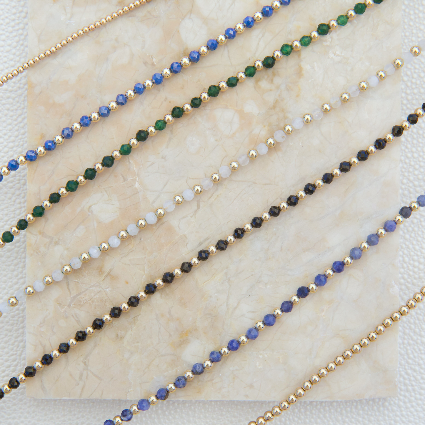 Display slab showcasing Gold Club by Shannon Hudson gemstone necklaces, including kyanite, white moonstone, green sandstone, blue zircon, and black onyx