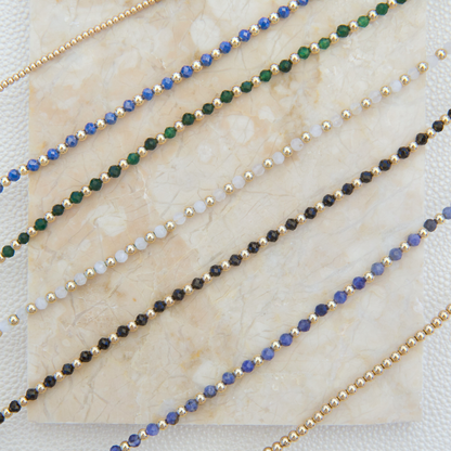 Display slab showcasing Gold Club by Shannon Hudson gemstone necklaces, including kyanite, white moonstone, green sandstone, blue zircon, and black onyx