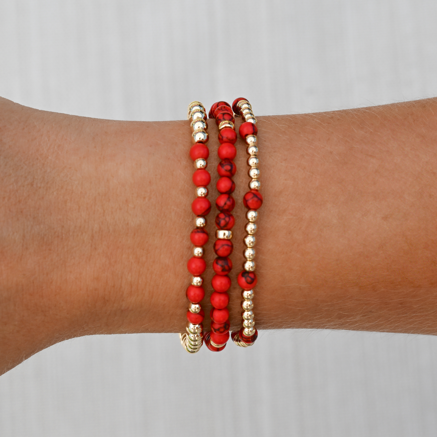 Red agate gemstone bracelets from GOLD CLUB by Shannon Hudson stacked on wrist, showcasing rich red tones with polished gold in a modern lifestyle setting.