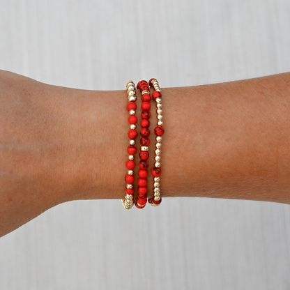 Red agate gemstone bracelets from GOLD CLUB stacked on wrist, showcasing rich red tones with polished gold in a modern lifestyle setting.