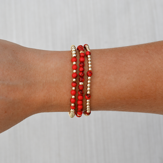 Red agate gemstone bracelets from GOLD CLUB stacked on wrist, showcasing rich red tones with polished gold in a modern lifestyle setting.