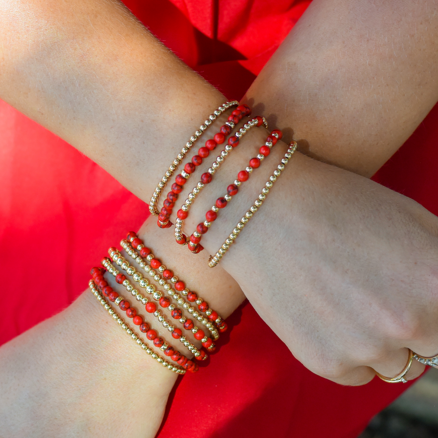 Close-up of a wrist wearing multiple red and gold beaded bracelets styled on a woman wearing a red dress.