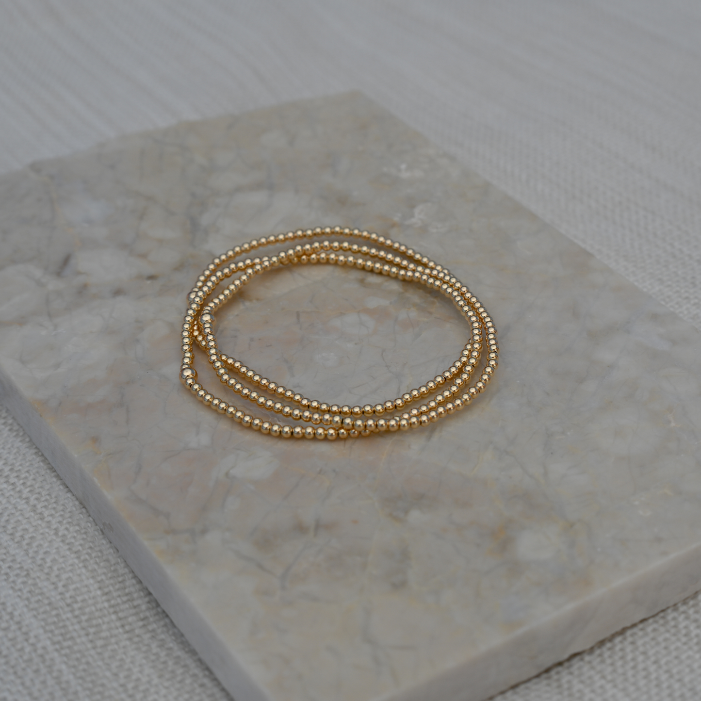 Set of three Gold Club by Shannon Hudson 2mm Gold LustraFlex™ Bracelet bracelets on a pretty tile