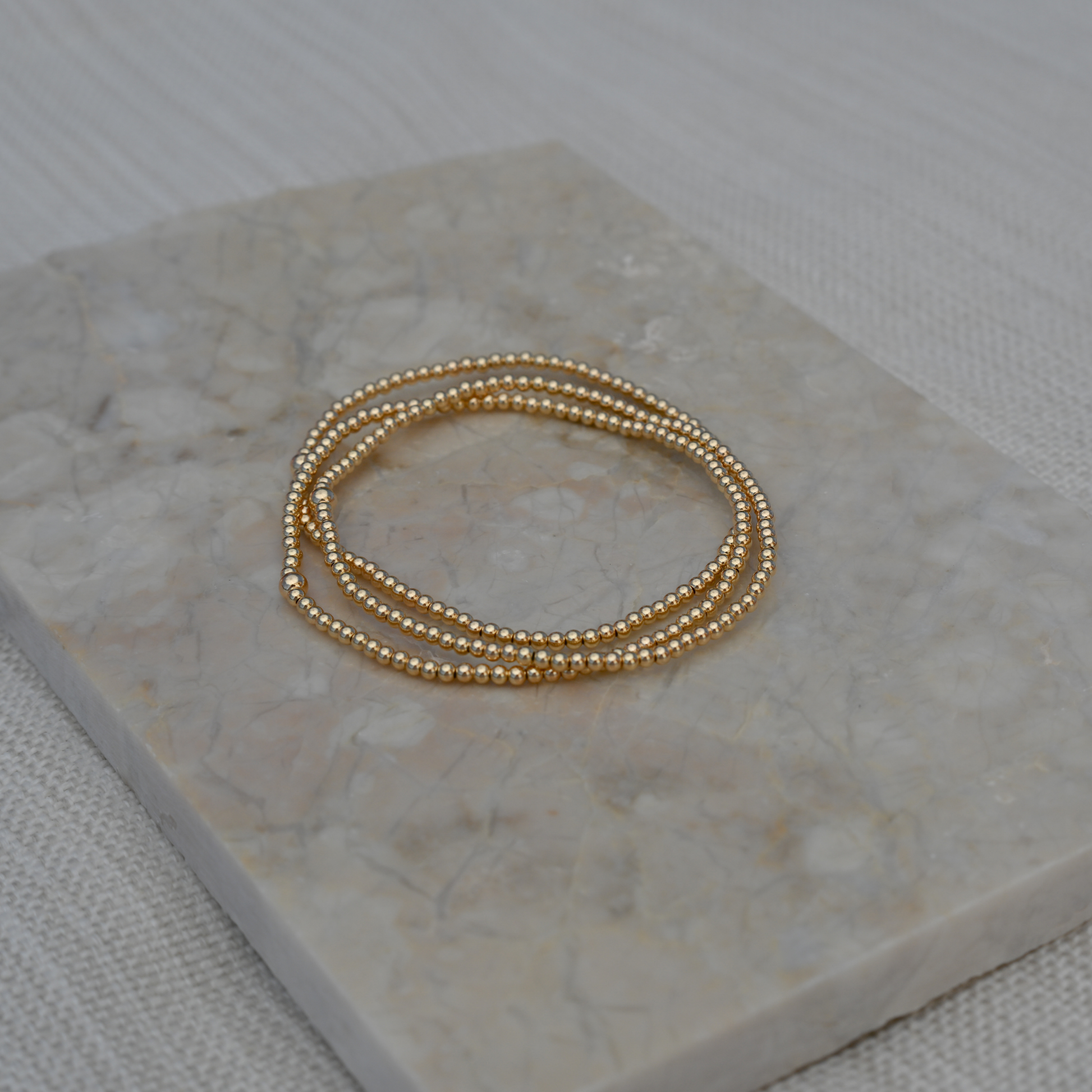 Set of three Gold Club by Shannon Hudson 2mm Gold LustraFlex™ Bracelet bracelets on a pretty tile